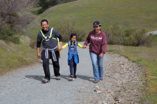 Man, child, and woman walking trail through green hills